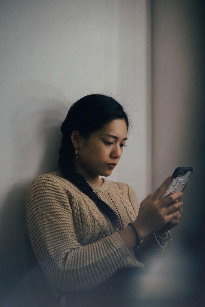 femme s'appuyant sur un mur blanc et utilisant un smartphone