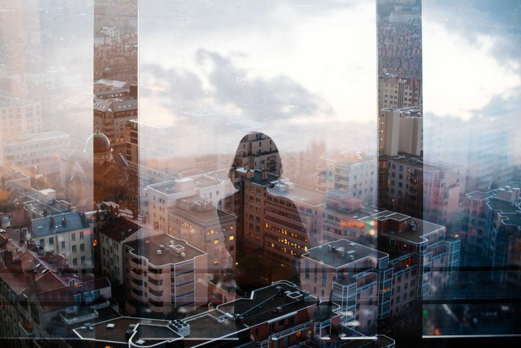 reflet d'une femme debout devant un panneau de verre faisant face à des immeubles de grande et moyenne hauteur