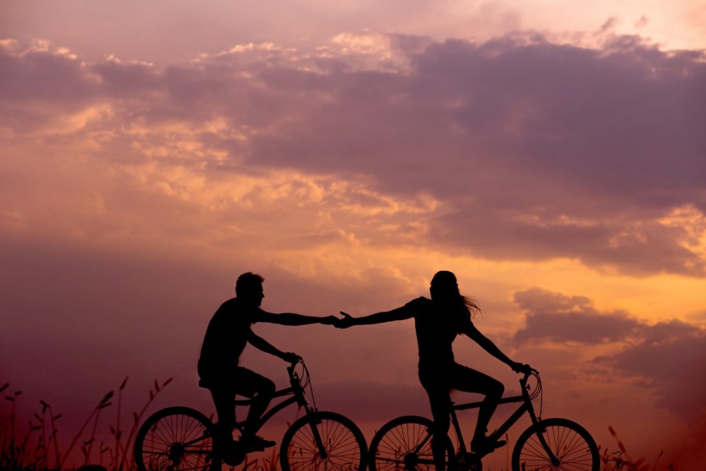 Une femme à vélo tend la main à un homme derrière elle, également à vélo.