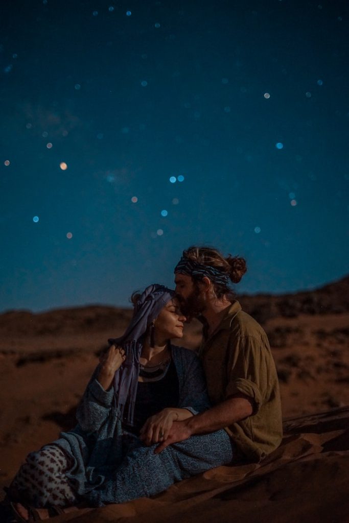 homme et femme assis sur le sable du désert sous un ciel bleu pendant la nuit