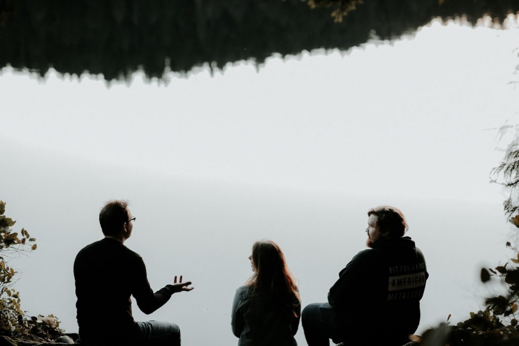 silhouette de trois personnes assises sur une falaise par temps brumeux