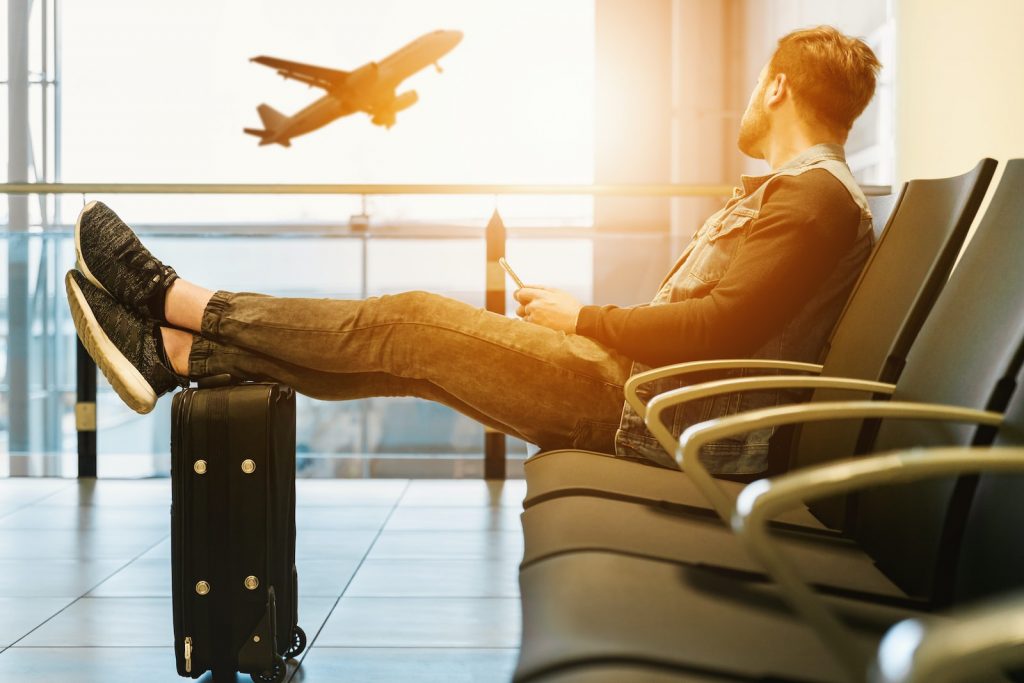 homme assis sur une chaise de gang, les pieds sur un bagage, regardant un avion