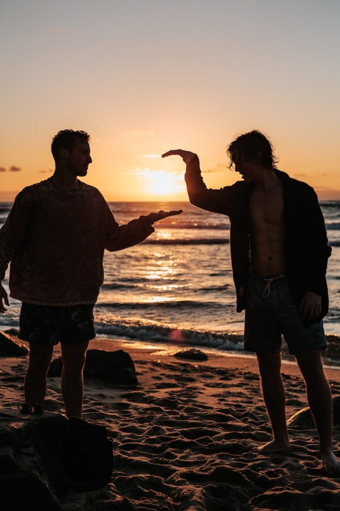 photo en gros plan de deux hommes se serrant la main près d'une plage au coucher du soleil