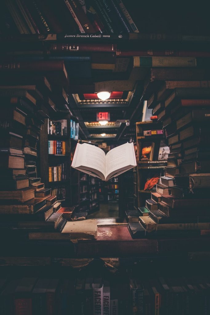 vue d'un livre ouvert flottant parmi des livres empilés dans une bibliothèque