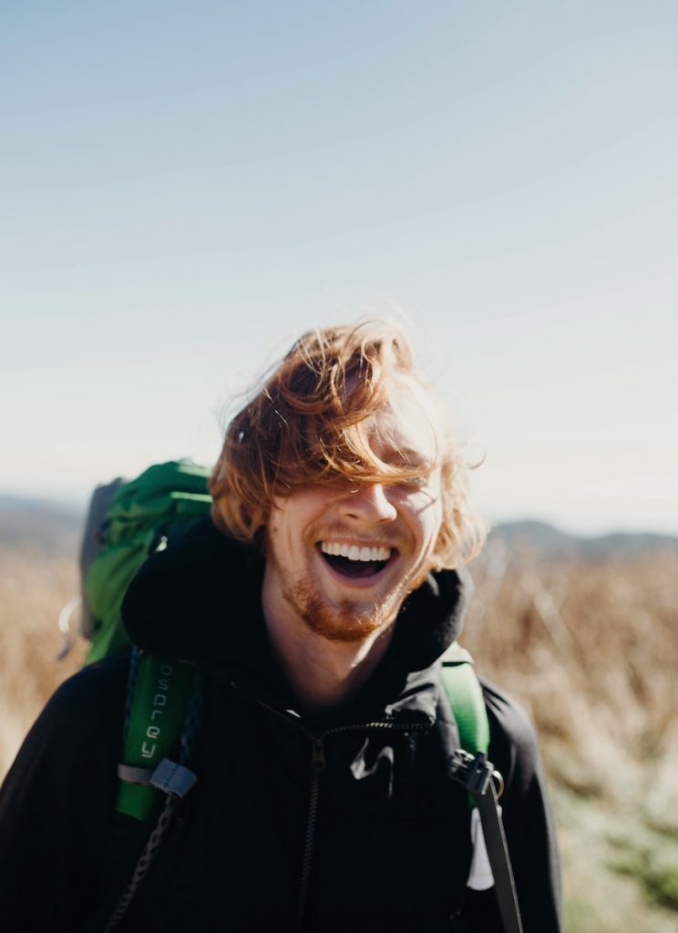 homme souriant avec un sac d'alpinisme vert pendant la journée
